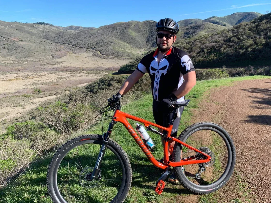 Eduardo Gutierrez standing with his mountain bike on a hillside trail
